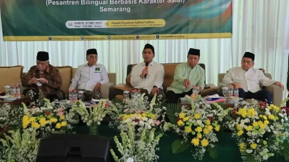 Lima pria mengenakan peci duduk di sofa, sebagian dikelilingi bunga.