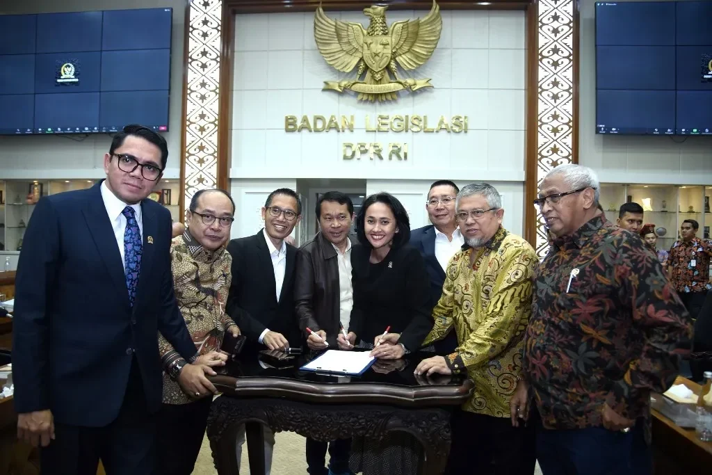 Delegasi Badan Legislasi DPR RI menandatangani dokumen resmi di depan lambang Garuda Pancasila.