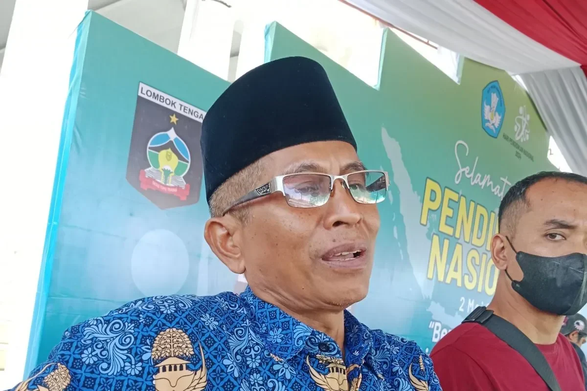 Pria berkacamata dan peci bicara di depan latar belakang spanduk pendidikan.