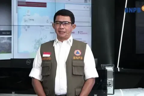 Pria mengenakan rompi coklat dengan logo BNPB dan bendera Indonesia.