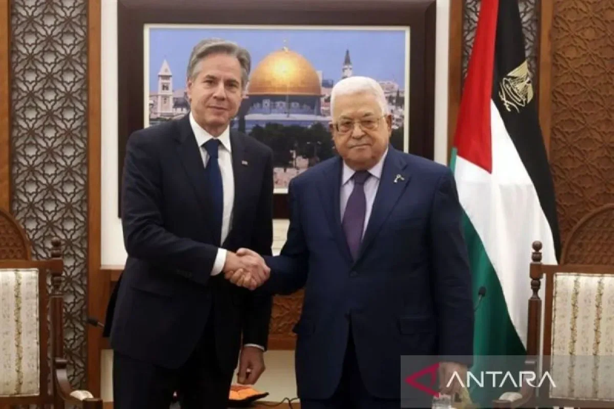 Presiden Palestina Mahmoud Abbas berjabat tangan dengan seorang diplomat, di depan bendera Palestina.