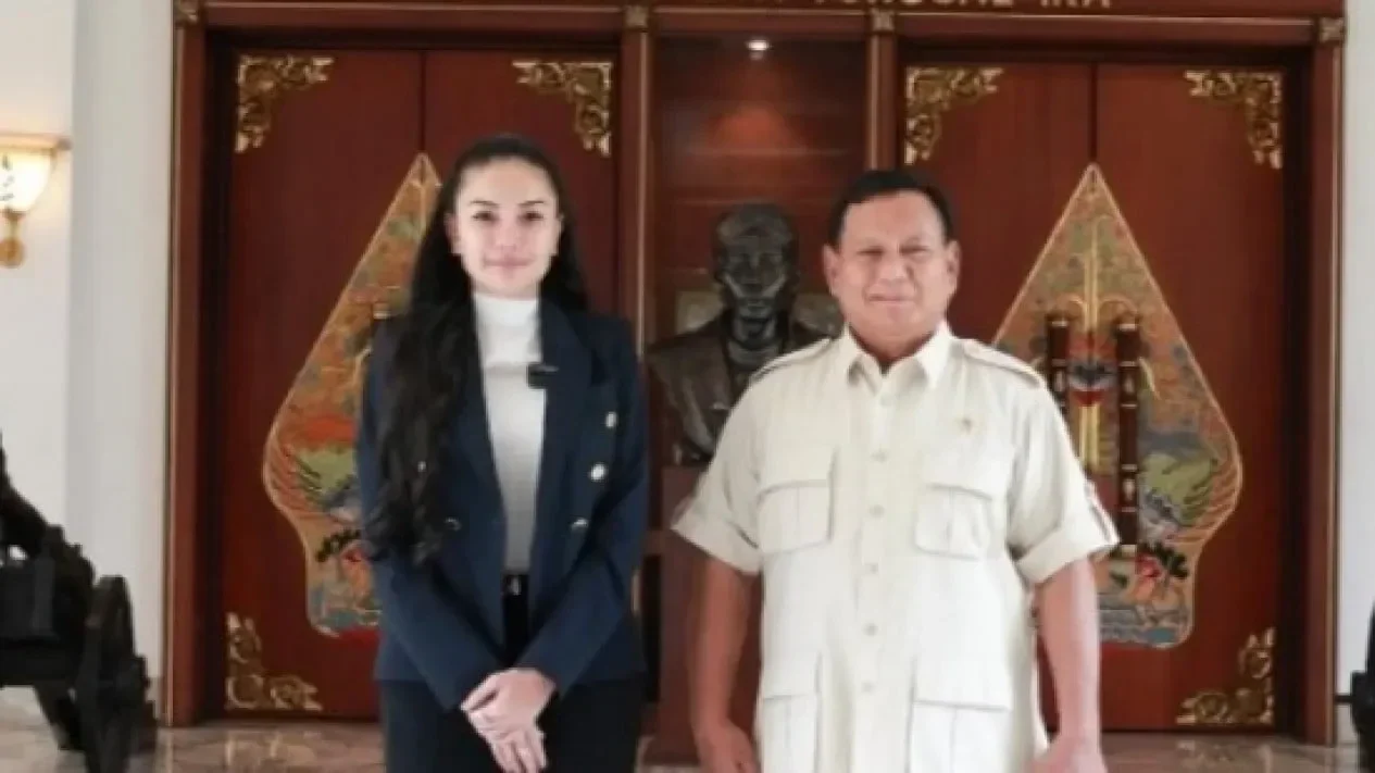 Presiden Prabowo Subianto tersenyum berkemeja krem, didampingi seorang wanita di sebuah acara.