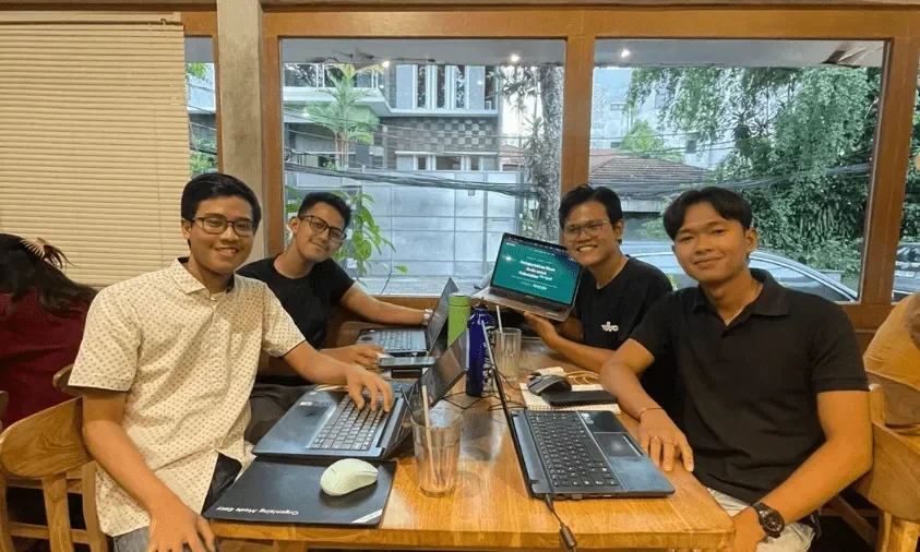 Empat generasi muda Indonesia berdiskusi sambil bekerja dengan laptop di sebuah kafe.