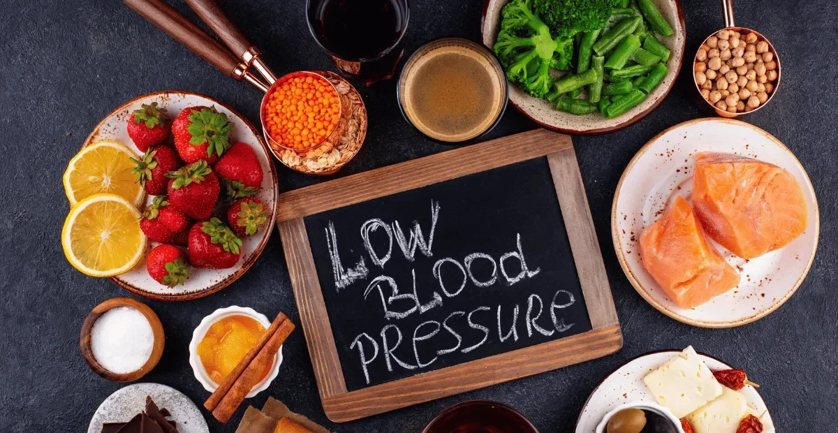 Papan hitam bertuliskan 'Low Blood Pressure' dikelilingi aneka makanan sehat dan bergizi.