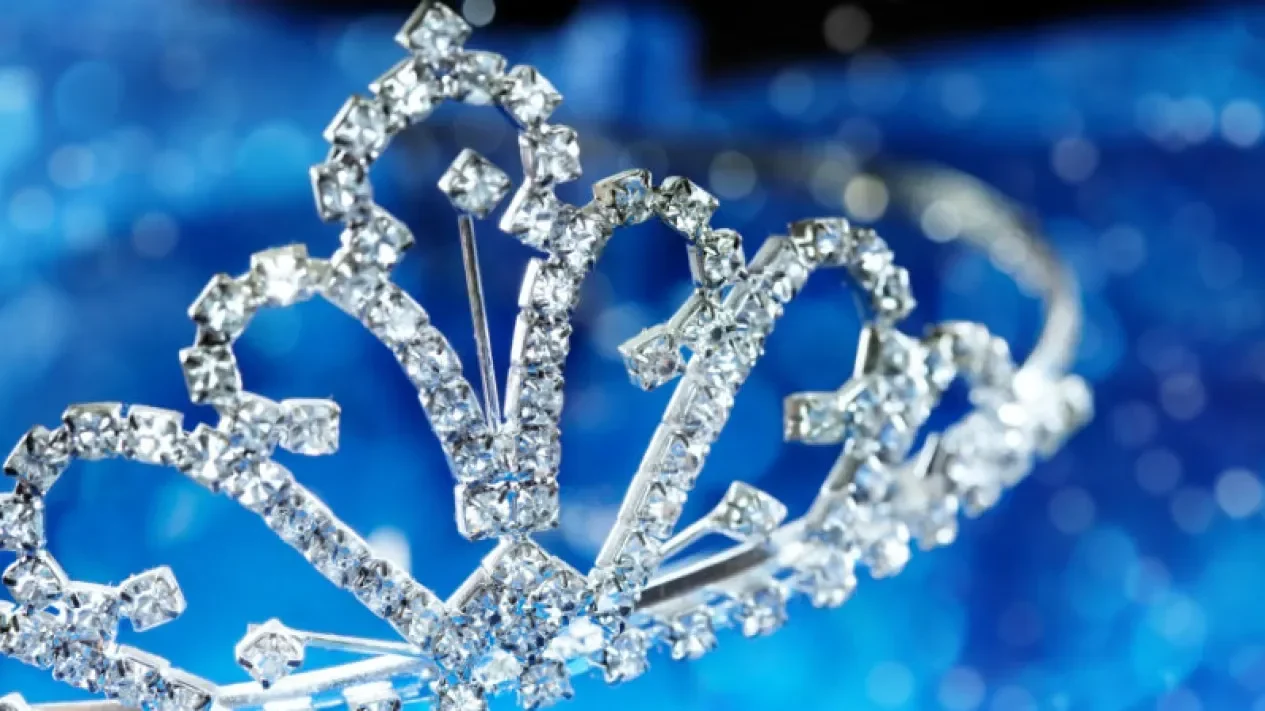 Mahkota berkilau bertatahkan permata, simbol kemenangan ratu kecantikan, di latar biru.