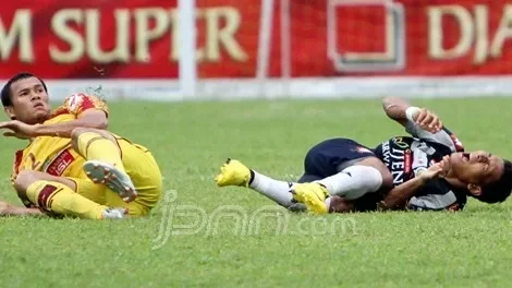 Dua pemain sepak bola terkapar di lapangan hijau setelah berbenturan.