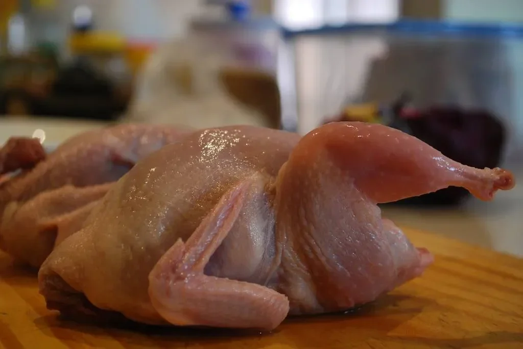 Dua ekor ayam mentah utuh tergeletak di atas talenan kayu.