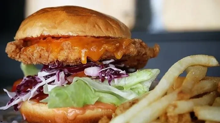 Burger ayam goreng dengan saus keju meleleh dan kentang goreng.