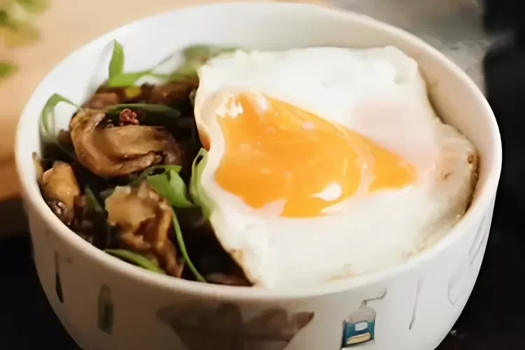 Semangkuk hidangan jamur tumis dengan telur mata sapi di atasnya.