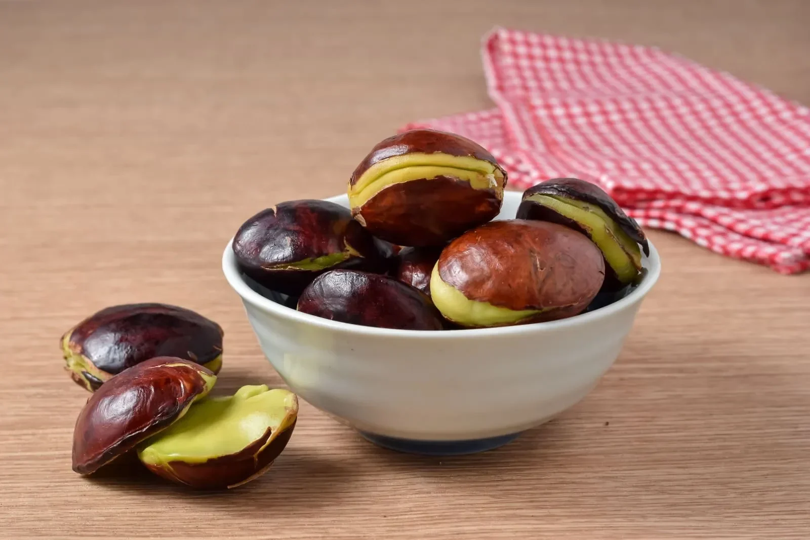 Secangkir jengkol matang di atas meja kayu, dengan serbet merah putih di latar belakang.