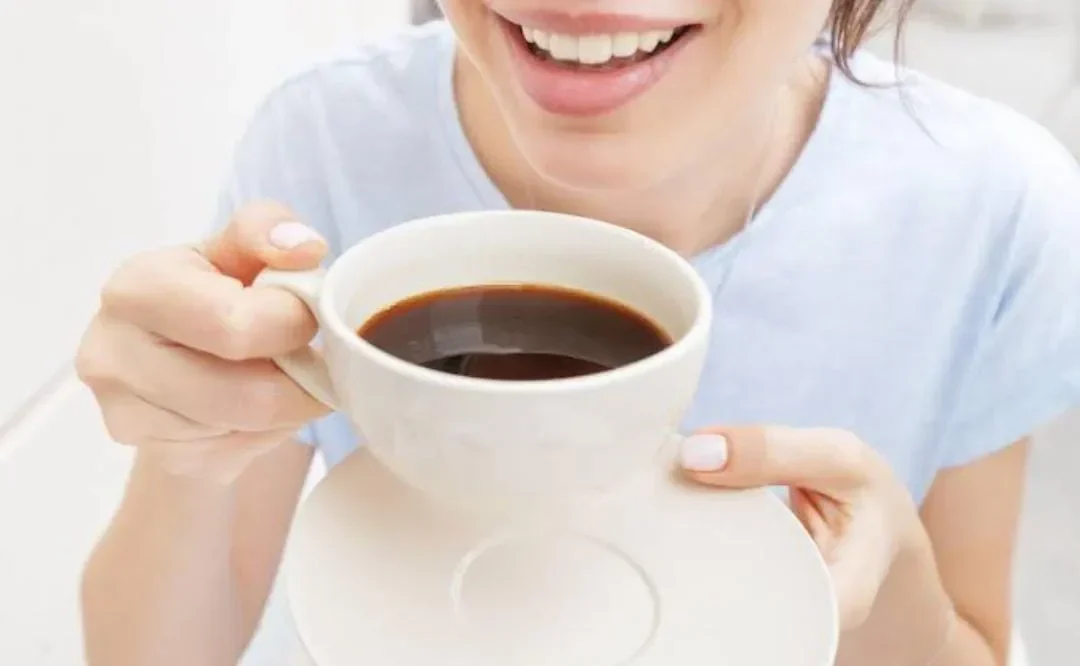 Wanita tersenyum memegang cangkir berisi kopi hitam.