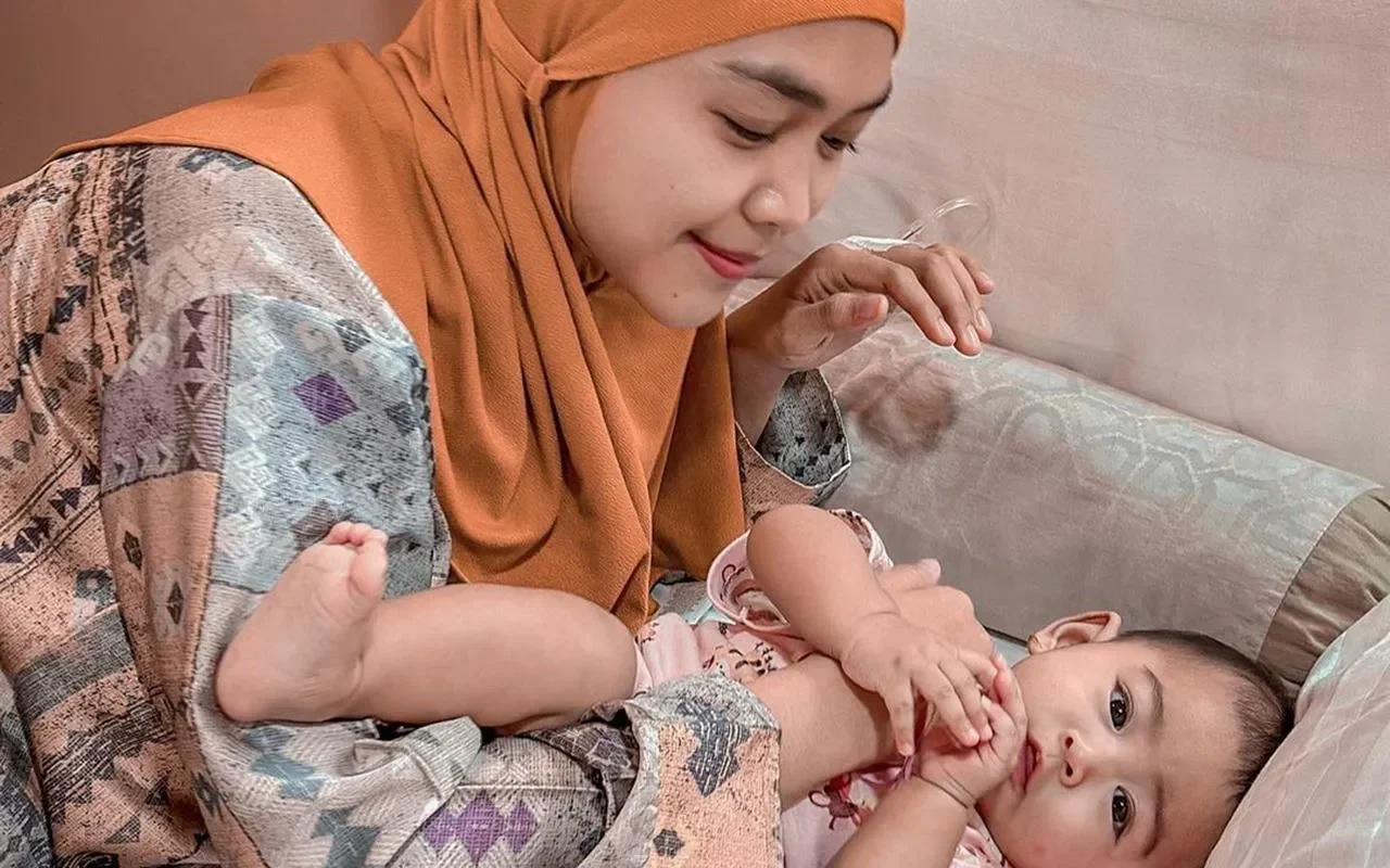 Wanita berkerudung oranye tersenyum melihat bayi dalam gendongannya di rumah sakit.