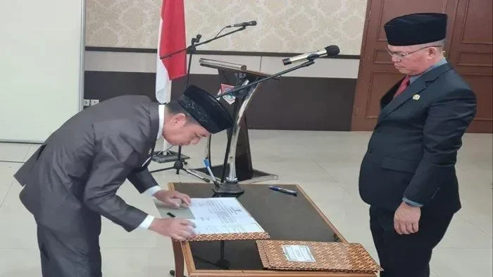 Pejabat menandatangani dokumen di depan bendera Indonesia saat acara resmi.