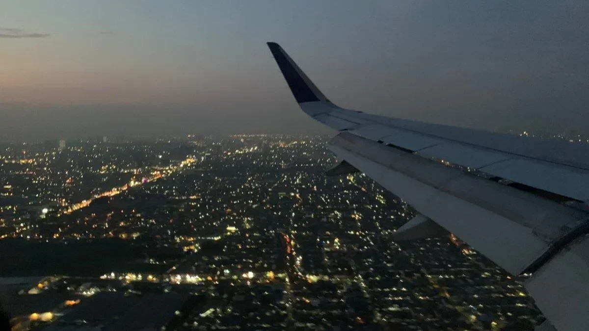 Pesawat terbang di atas pemandangan kota di malam hari.