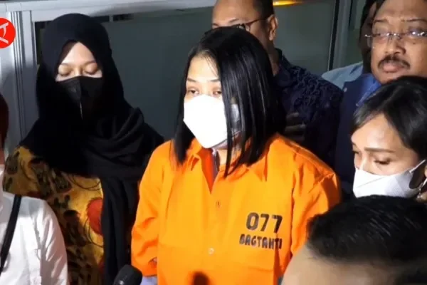 Wanita berkaos tahanan oranye bernomor 077 dan masker putih, dikelilingi sejumlah orang.