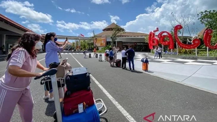 Turis tiba di bandara dengan koper, latar belakang logo "Bali Paradise" dan bangunan.