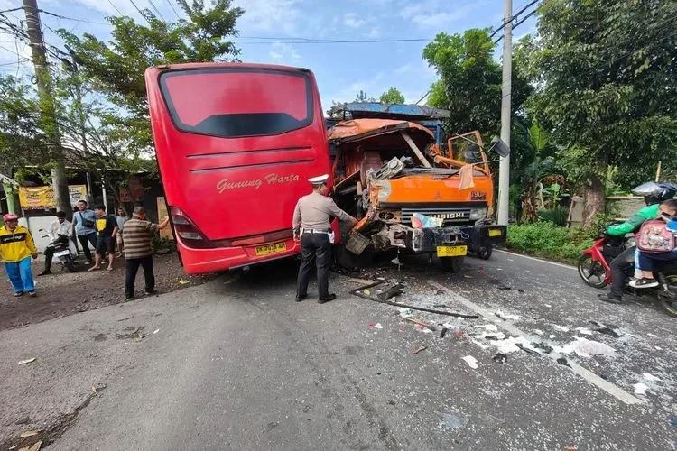 Kecelakaan bus dan truk dengan kerusakan parah, petugas polisi di lokasi.