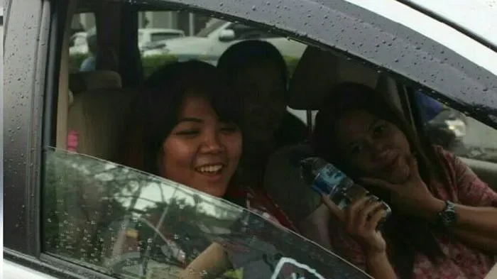 Tiga orang wanita tersenyum di dalam mobil dengan latar belakang hujan.