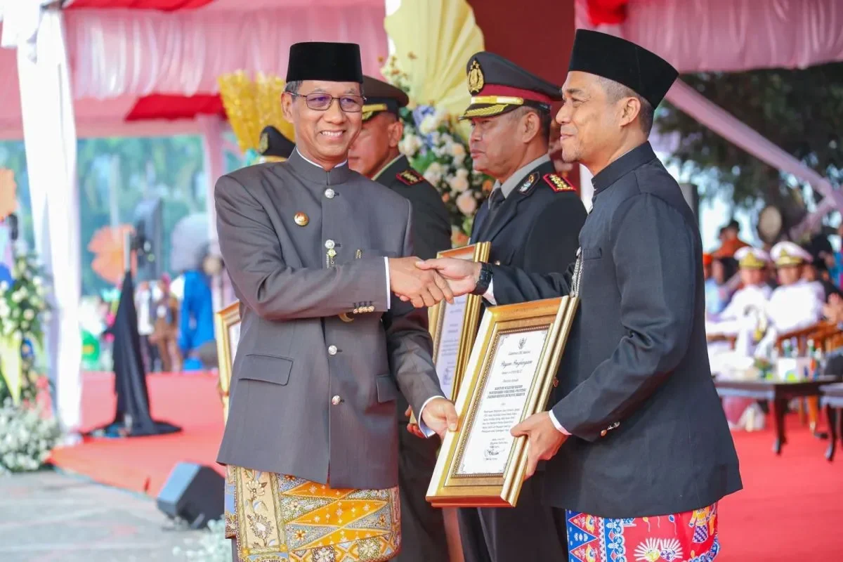 Pejabat berjabat tangan dan menyerahkan piagam dalam acara formal.