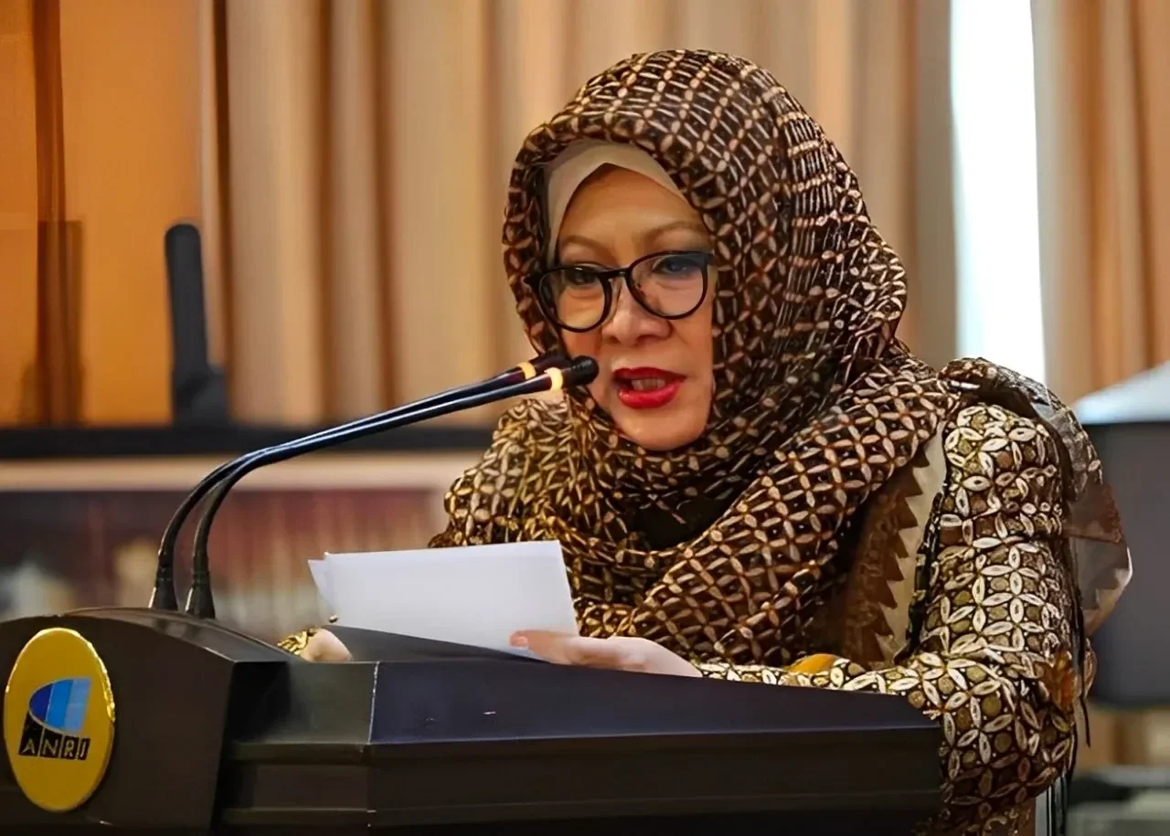 Tutut Soeharto mengenakan hijab dan pakaian bermotif saat berbicara di podium dengan mikrofon.