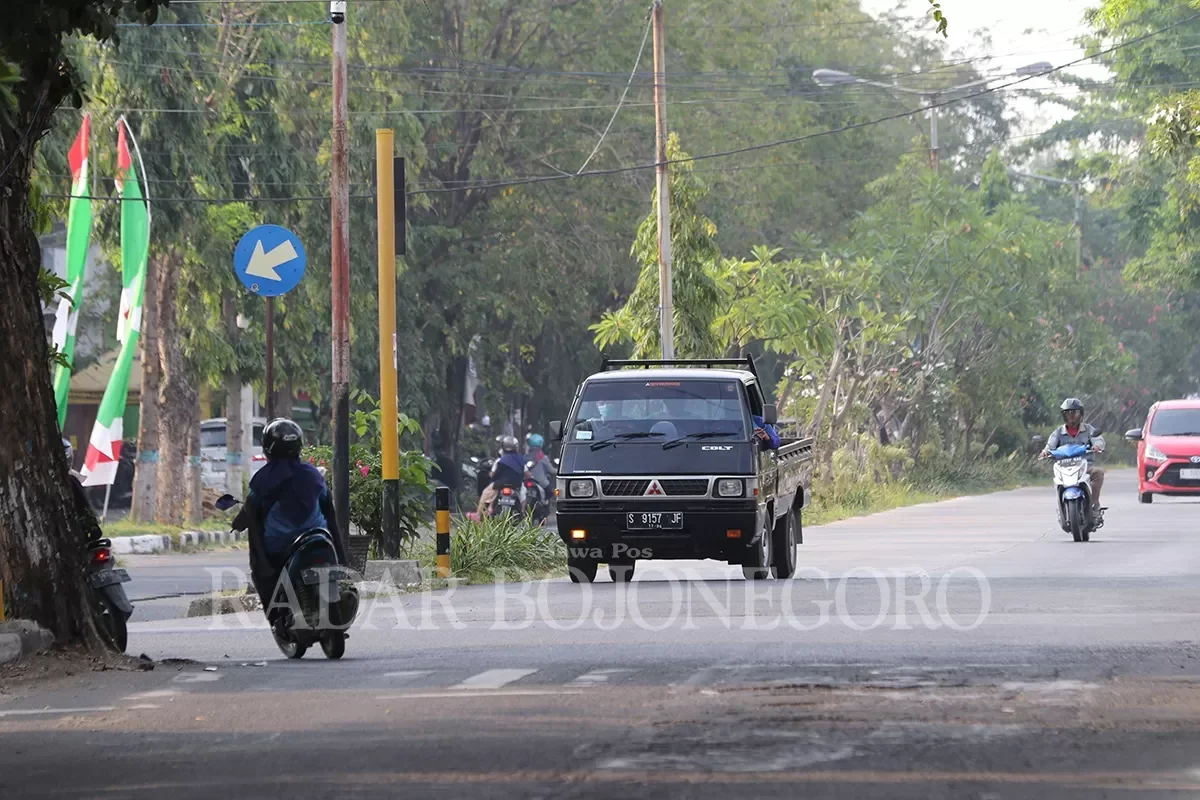 Sebuah mobil pikap hitam melaju di jalan raya yang dikelilingi pepohonan.