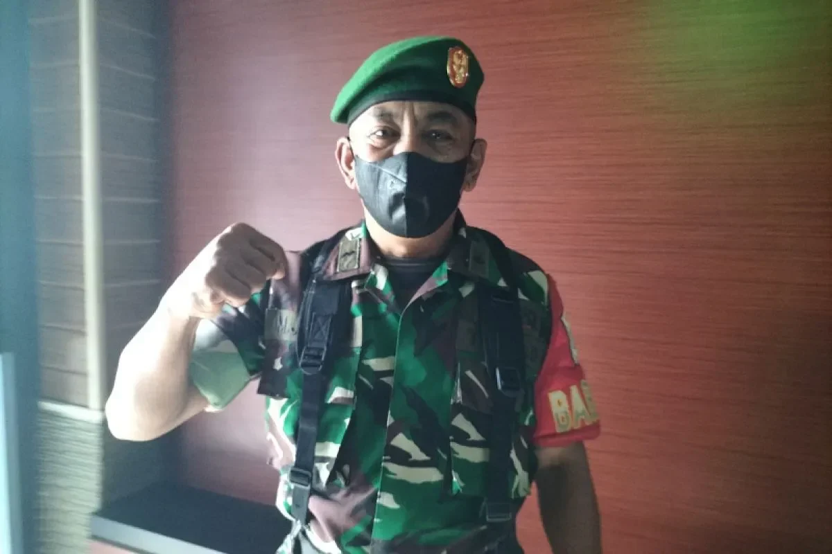 Seorang pria berseragam militer, memakai masker, menunjukkan kepalan tangan sebagai simbol kekuatan.