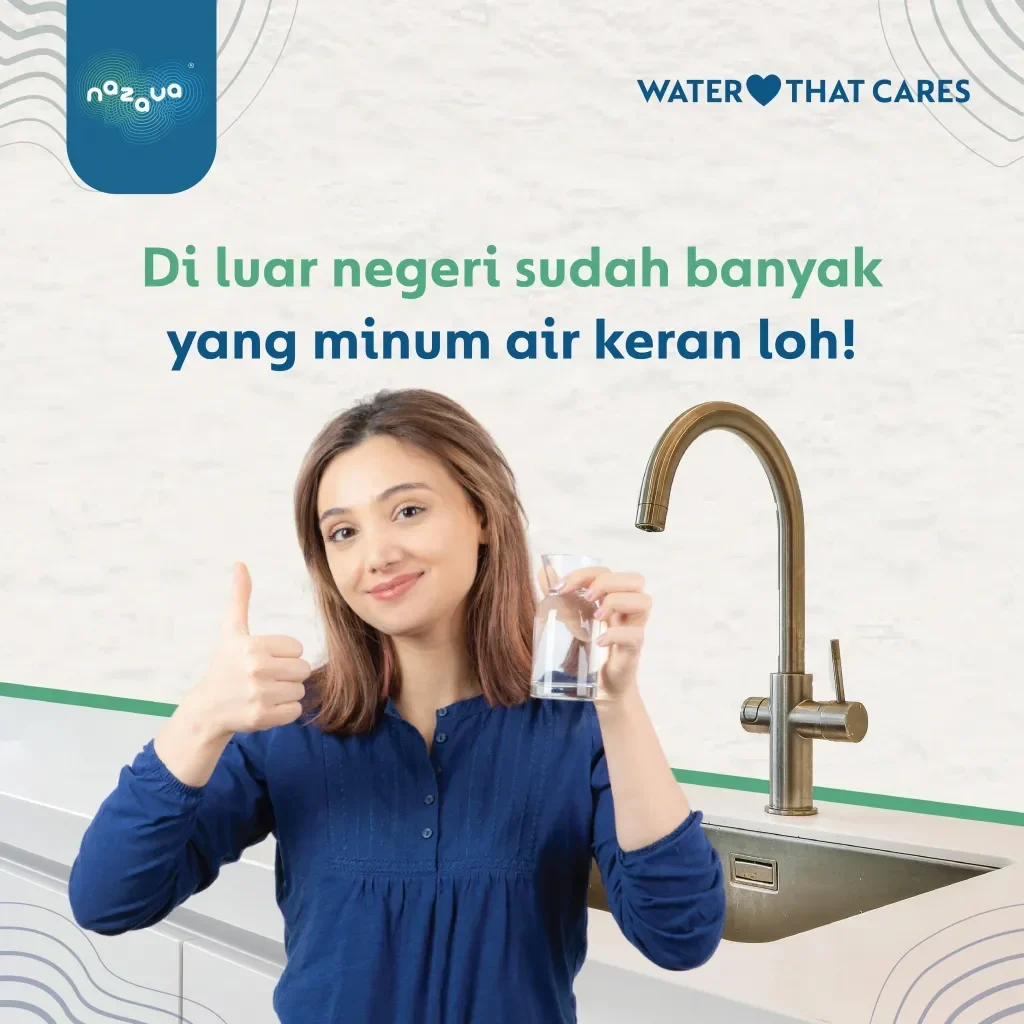 Wanita tersenyum memegang gelas air minum di depan keran.