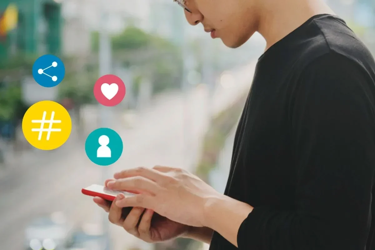 Seorang menggunakan ponsel dengan ikon berbagi, suka, tagar, dan profil media sosial.