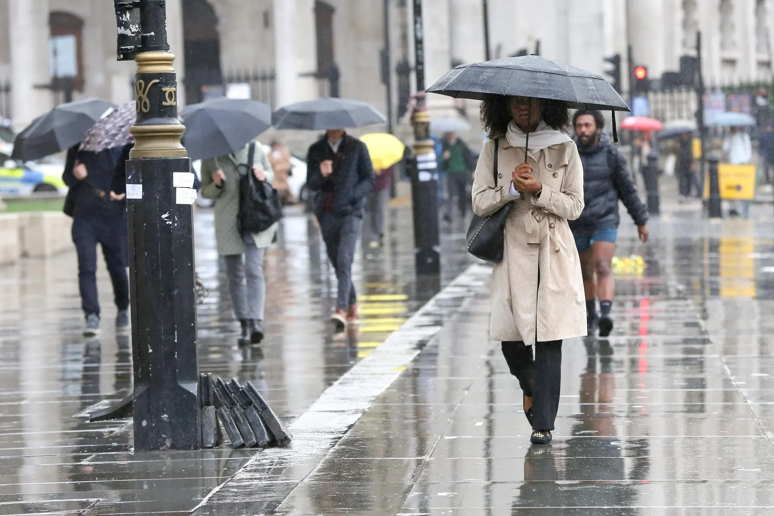 Pejalan kaki di kota menggunakan payung di tengah guyuran hujan lebat.