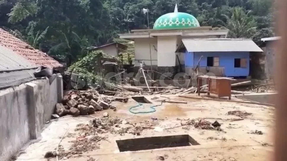 Sisa-sisa puing-puing dan lumpur setelah bencana banjir, dengan bangunan dan masjid di latar belakang.