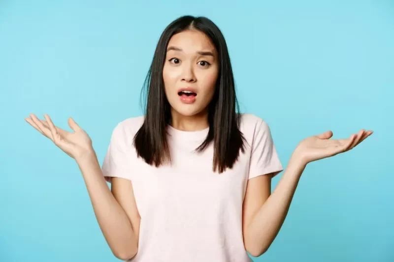 Wanita bingung mengangkat tangan dengan ekspresi kaget di latar belakang biru.