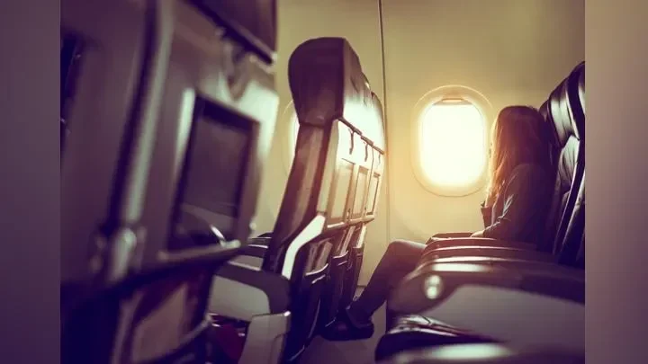 Penumpang wanita duduk sendiri di kursi pesawat dekat jendela, menikmati ruang ekstra.