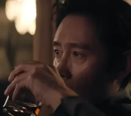 Lee Byung-hun memegang gelas, tatapan penuh makna di film No Other Choice.