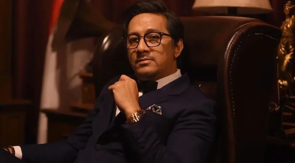 Andre Taulany duduk di kursi kulit, memakai setelan jas, tatapan serius.