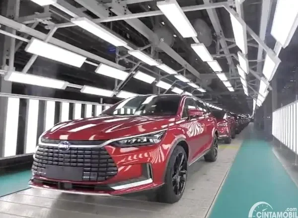 Mobil listrik berwarna merah di lini produksi pabrik otomotif dengan lampu terang.