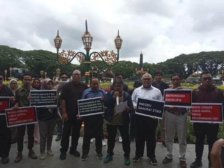 Sekelompok orang memegang poster protes di depan gedung dengan pilar.
